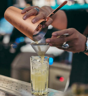 Bartender straining a cocktail into a tall glass filled with ice