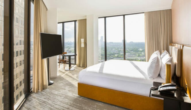 Corner room with king bed, floor to ceiling windows, flat screen TV mounted on a stand, and seating area