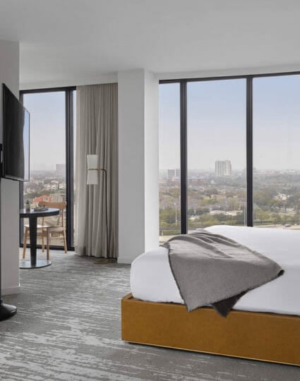 Corner room with king bed, floor to ceiling windows, flat screen TV mounted on a stand, and seating area