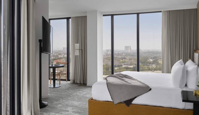 Corner room with king bed, floor to ceiling windows, flat screen TV mounted on a stand, and seating area