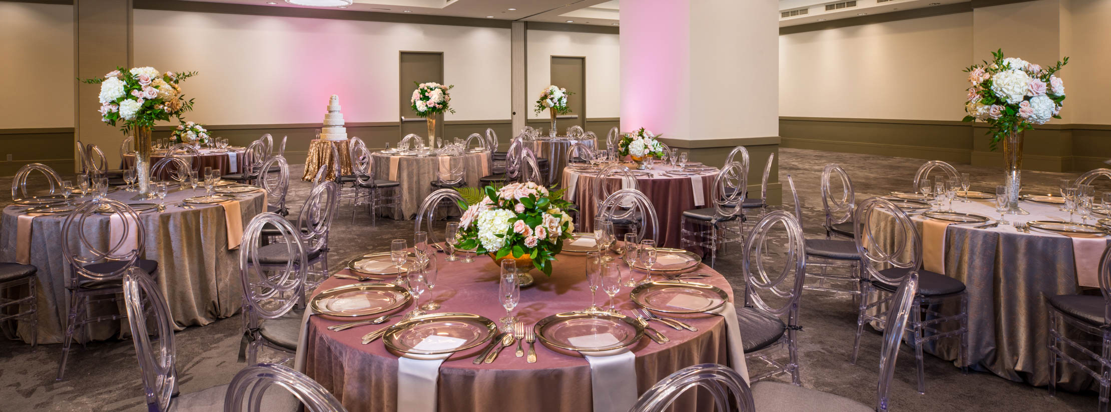 Dezavala banquet room with seven round banquet tables with eight seats each, adorned with rose table cloths and various floral centerpieces