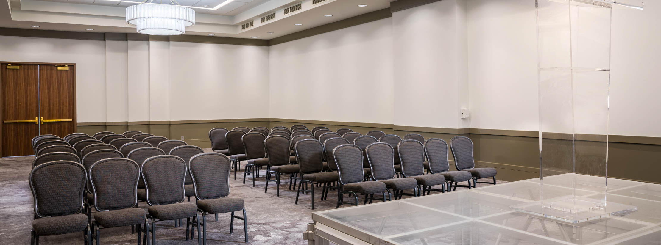 Smaller Dezavala room configured with a raised stage and podium in front of rows of chairs with center aisle