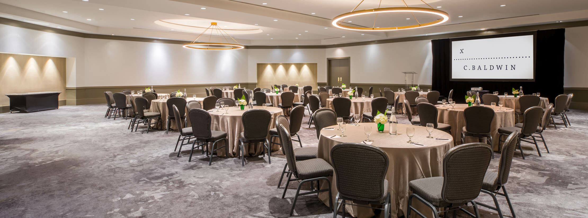 Jordan ballroom with large round tables, screen for presentations, and podium for spreaches