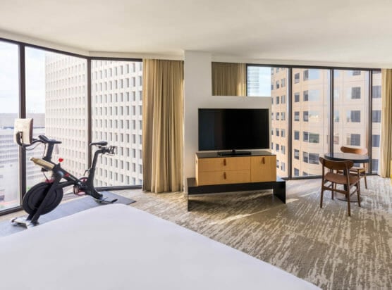 Large room with flat-screen tv on entertainment center, small sitting table and peloton bike