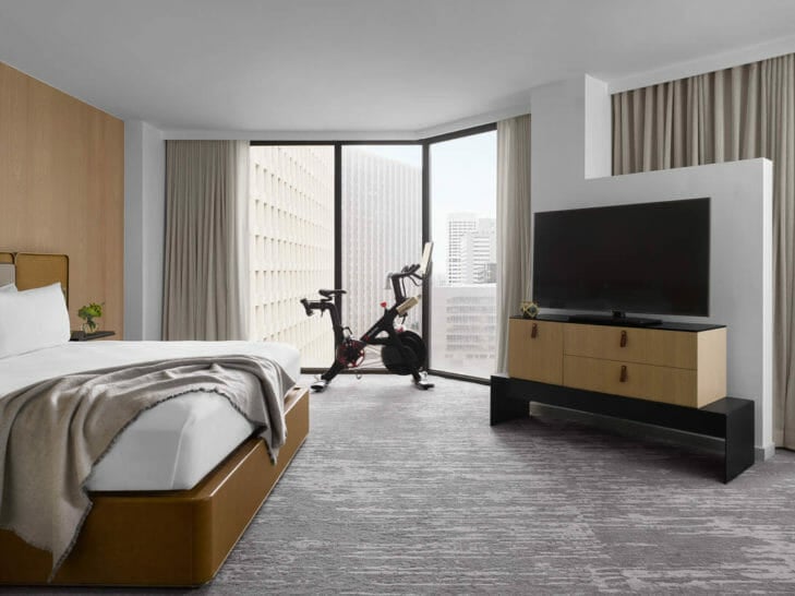 Large room with flat-screen tv on entertainment center, small sitting table and peloton bike