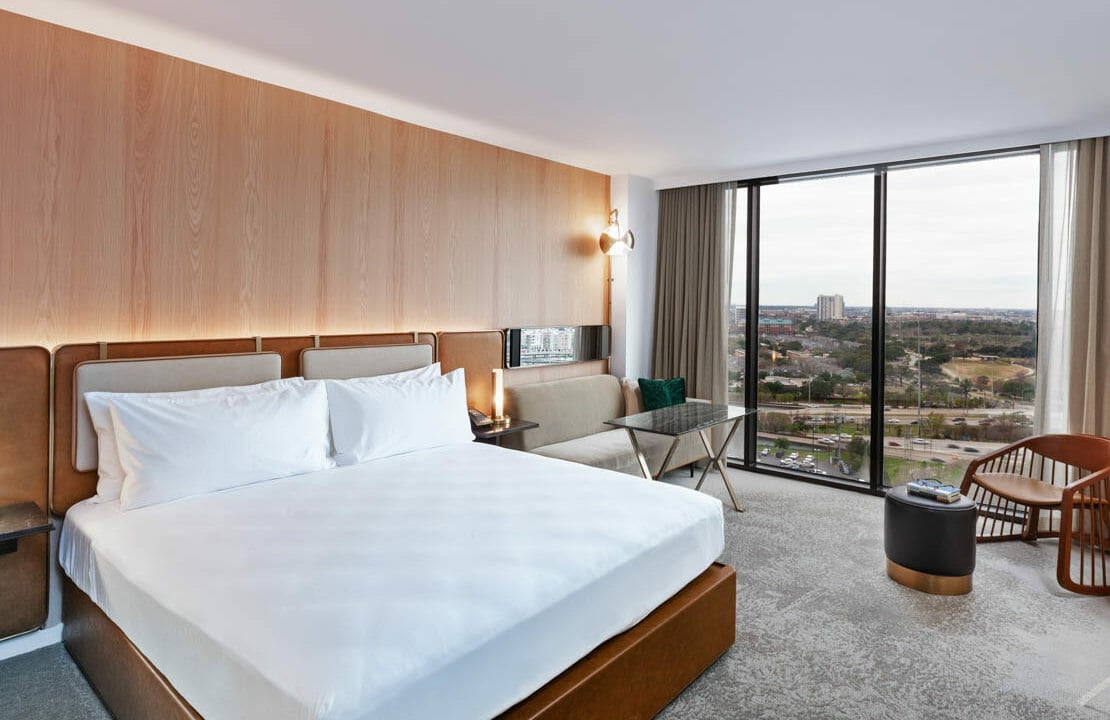 King sized bed room with seating area that includes view of Houston through floor to ceiling windows.