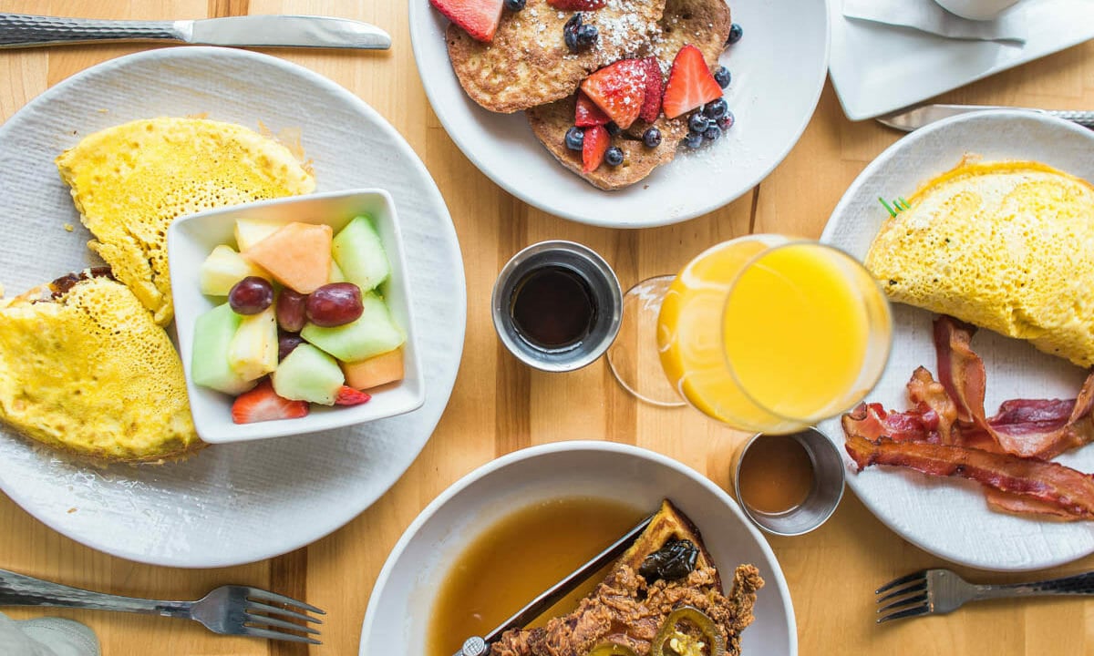 Top down view of four breakfast plates such as pancakes, omelette and bacon, french toast, and chicken and waffles