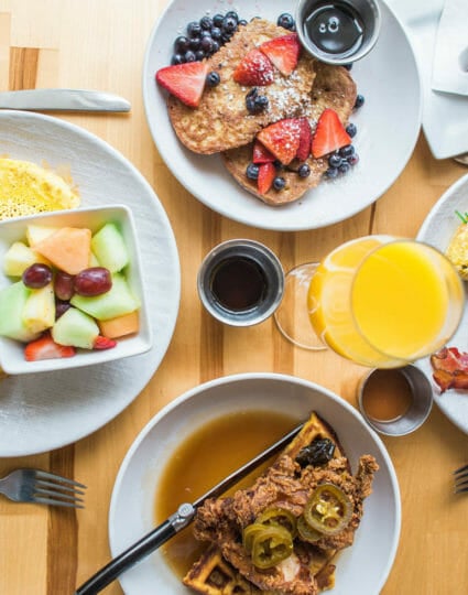 Top down view of four breakfast plates such as pancakes, omelette and bacon, french toast, and chicken and waffles