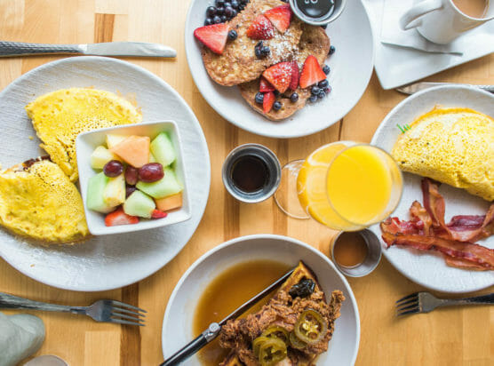 Top down view of four breakfast plates such as pancakes, omelette and bacon, french toast, and chicken and waffles
