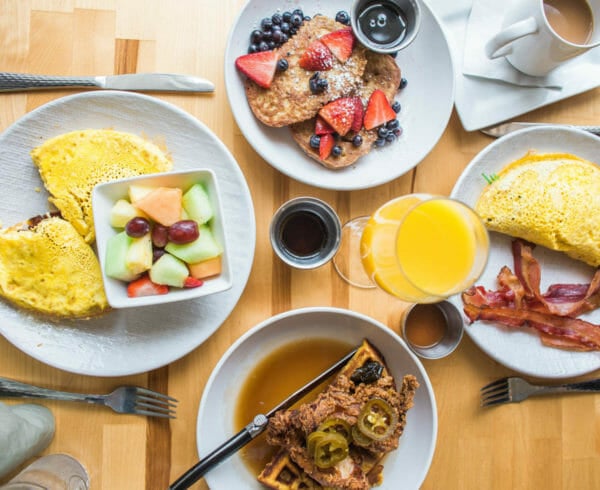 Top down view of four breakfast plates such as pancakes, omelette and bacon, french toast, and chicken and waffles