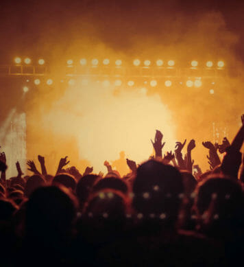 Concert goers enjoying a band preforming on stage under bright yellow stage lights