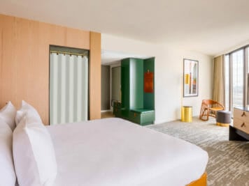 King bed and entry way of room with part of the closet space and floor to ceiling windows opposite the bed
