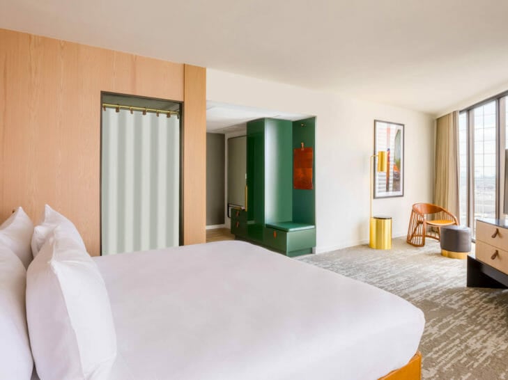 King bed and entry way of room with part of the closet space and floor to ceiling windows opposite the bed