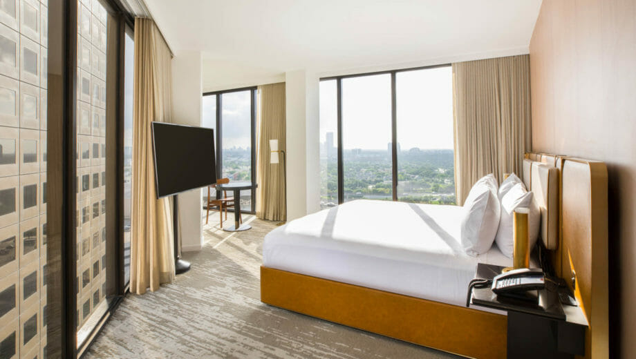 Corner room with king bed, floor to ceiling windows, flat screen TV mounted on a stand, and seating area