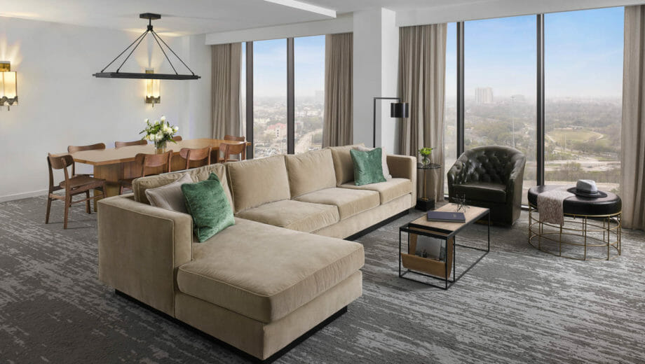 Spacious Presidential Suite living room with floor to ceiling windows, tan sectional in seating area and dining table behind it.