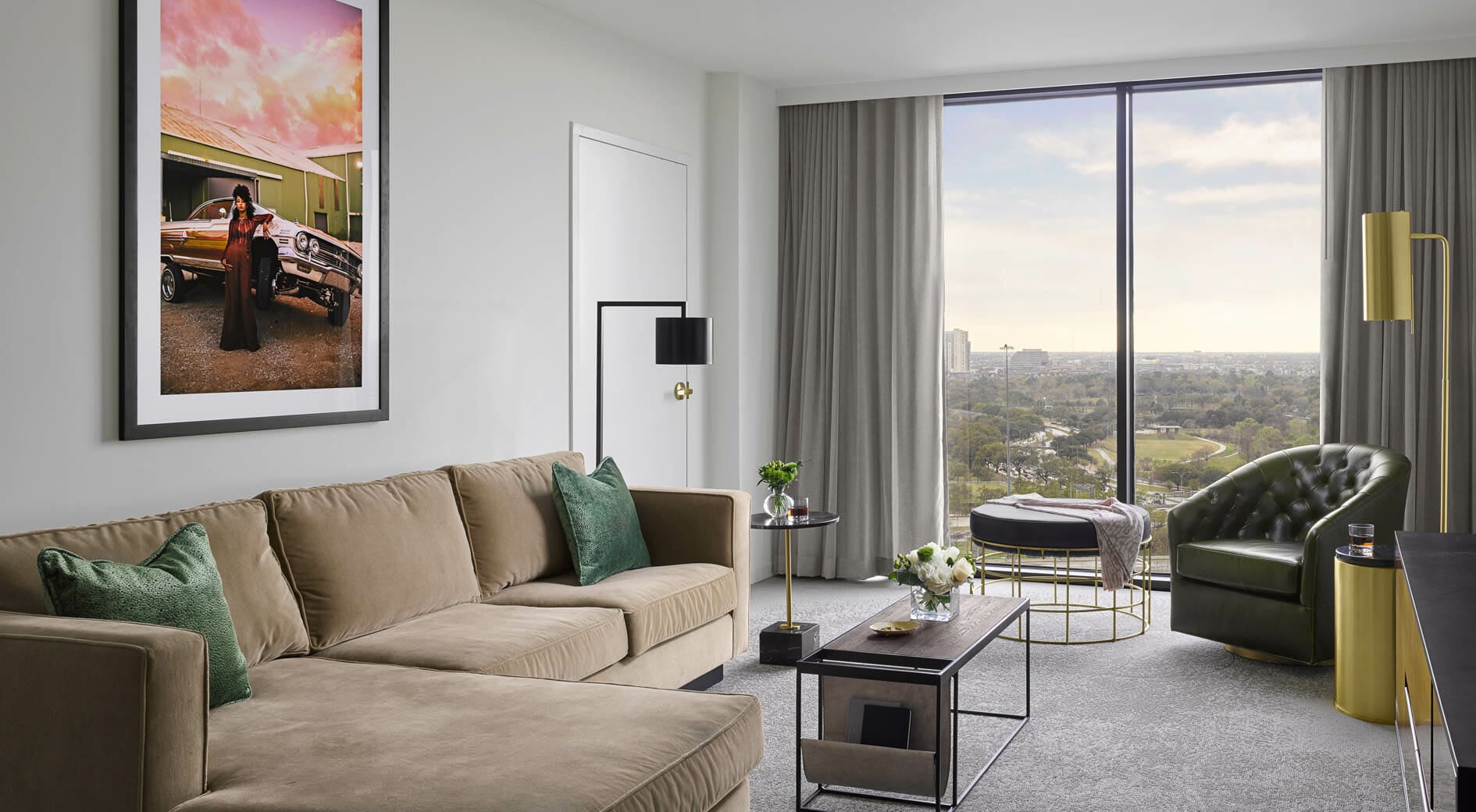Spacious Presidential Suite living room with floor to ceiling windows, tan sectional in seating area and dining table behind it.