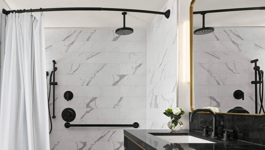 Spacious accessible shower with black fixtures and white curtain.