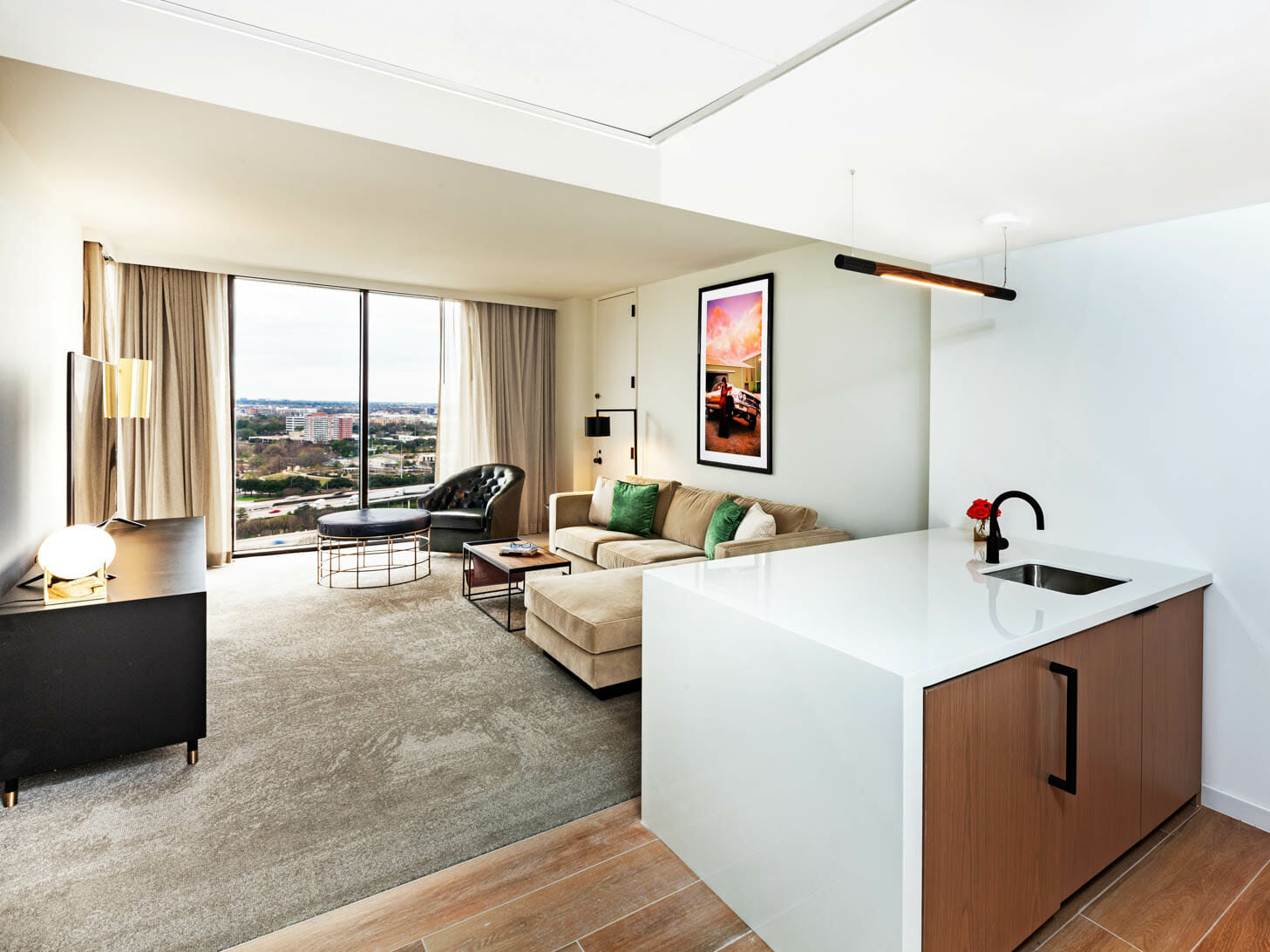 Spacious Presidential Suite living room with floor to ceiling windows, tan sectional in seating area and dining table behind it.