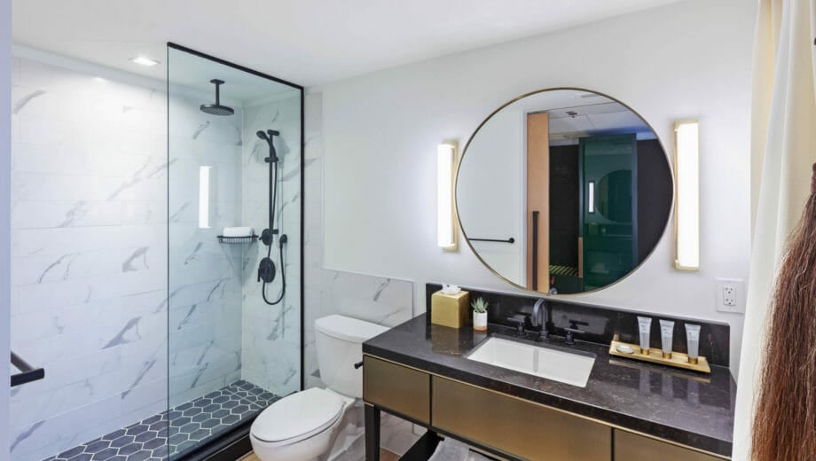 Bathroom with stand up shower, toilet, and vanity with circular mirror