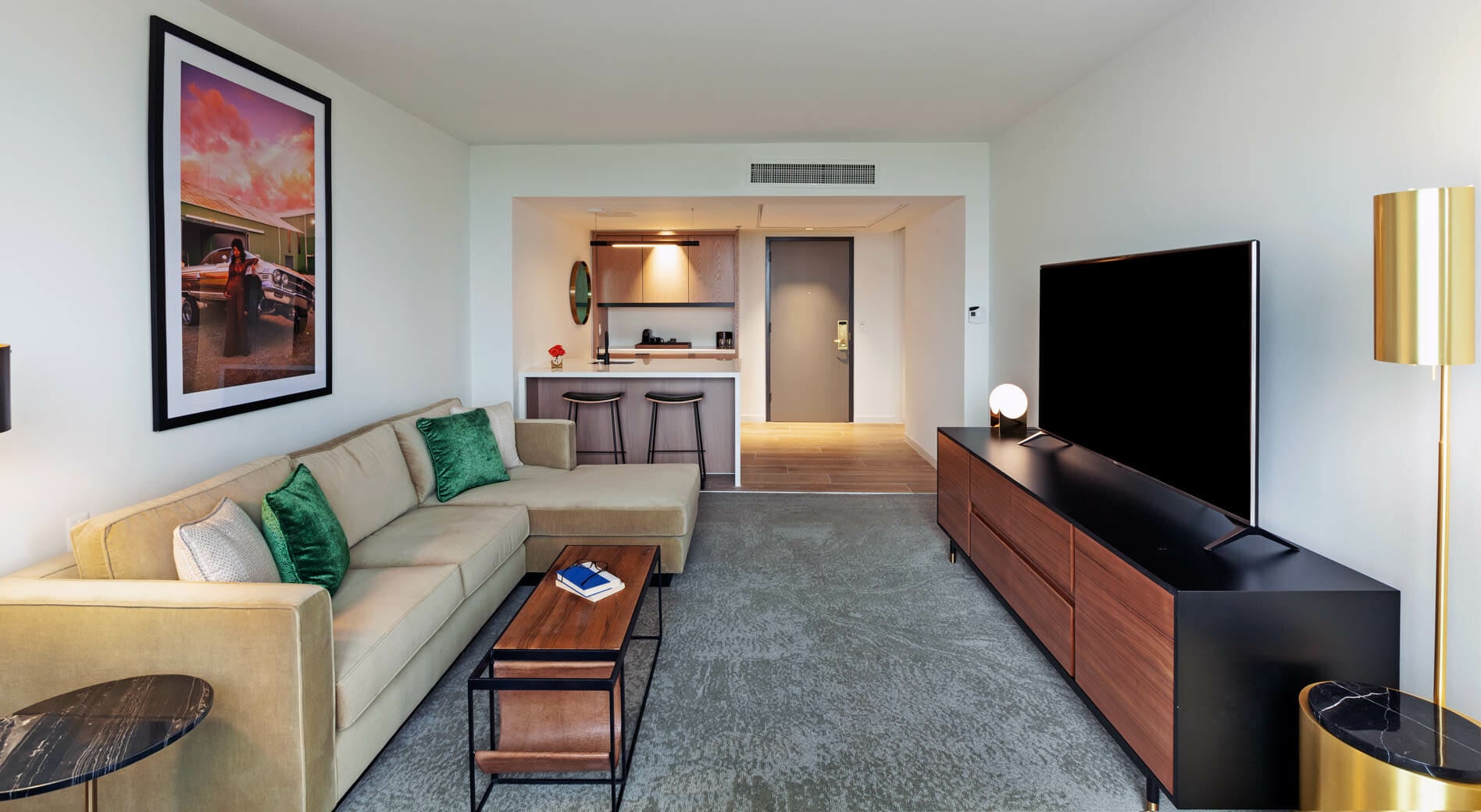 Spacious Presidential Suite living room with floor to ceiling windows, tan sectional in seating area and dining table behind it.