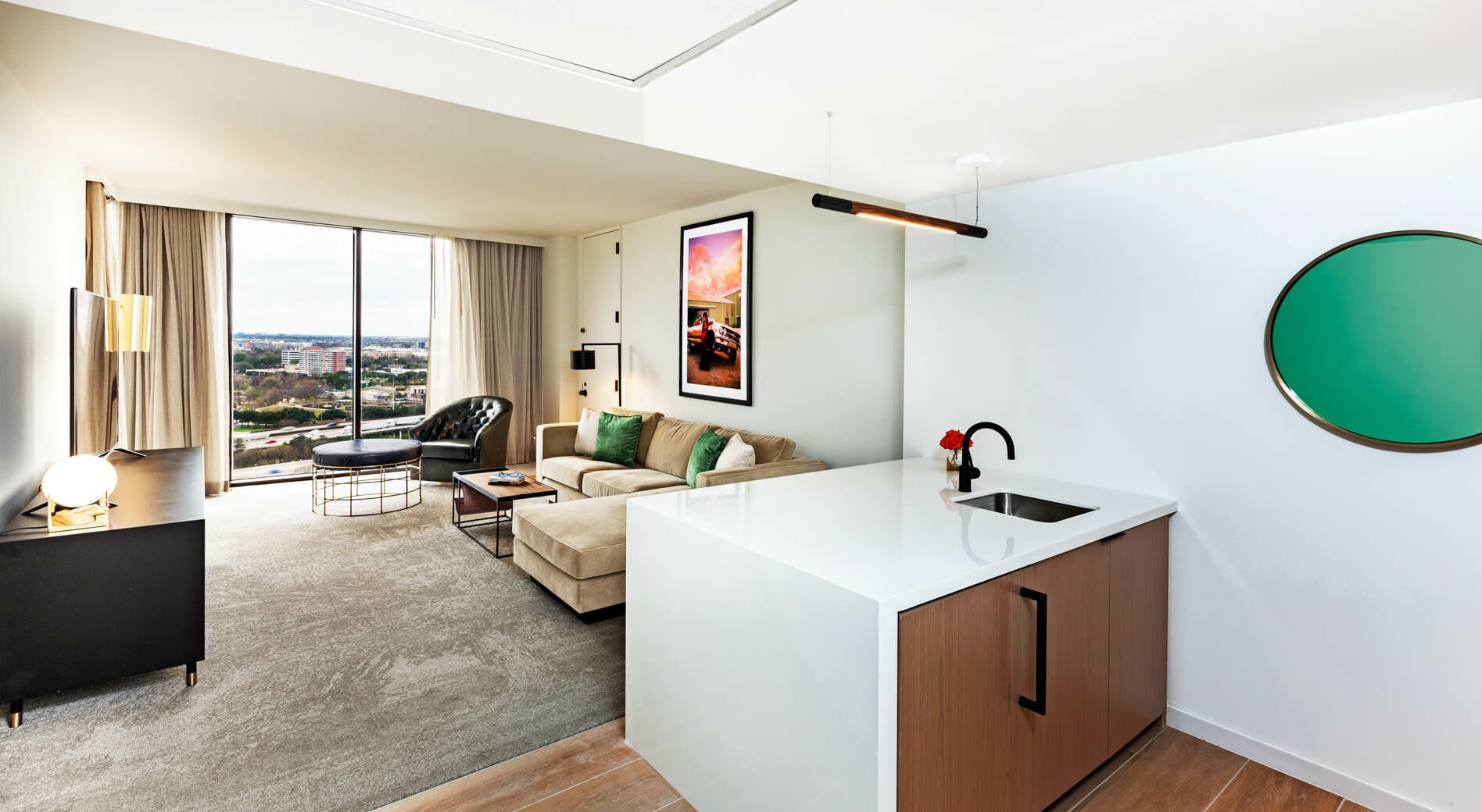 Spacious Presidential Suite living room with floor to ceiling windows, tan sectional in seating area and dining table behind it.