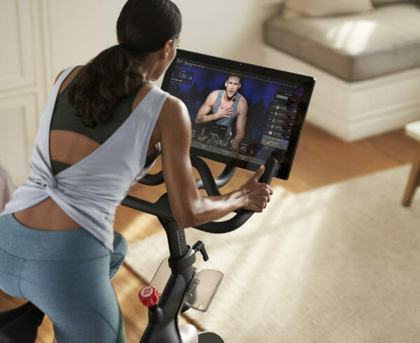 A woman on a peleton taking a class with an instructor on screen