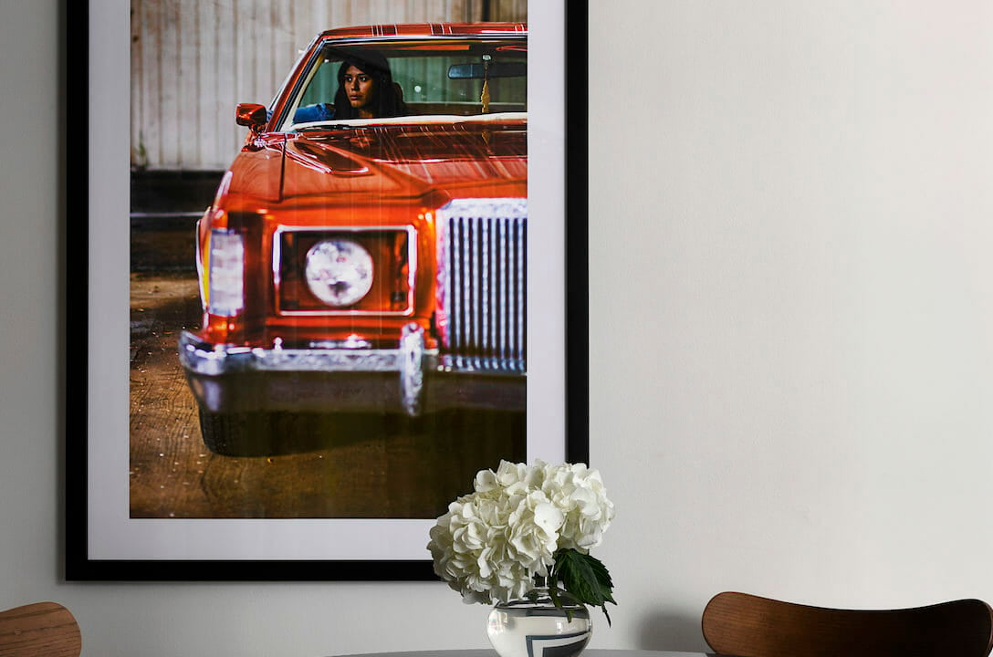 A close up of a dining room table with a picture of a woman in a red car on the wall