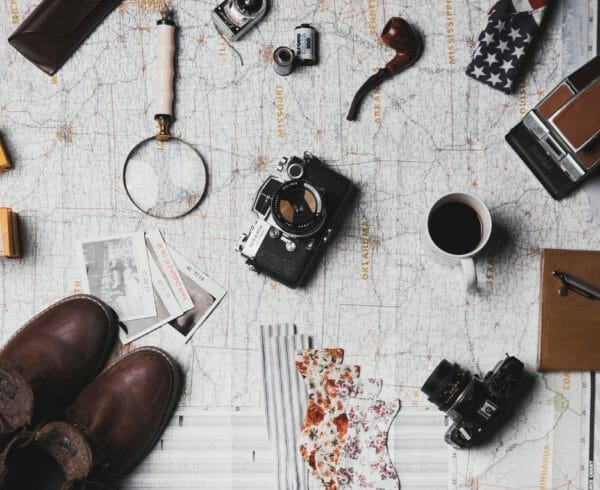 A map with knick knacks like cameras, spy glass, brown shoes and a pipe on top of it.