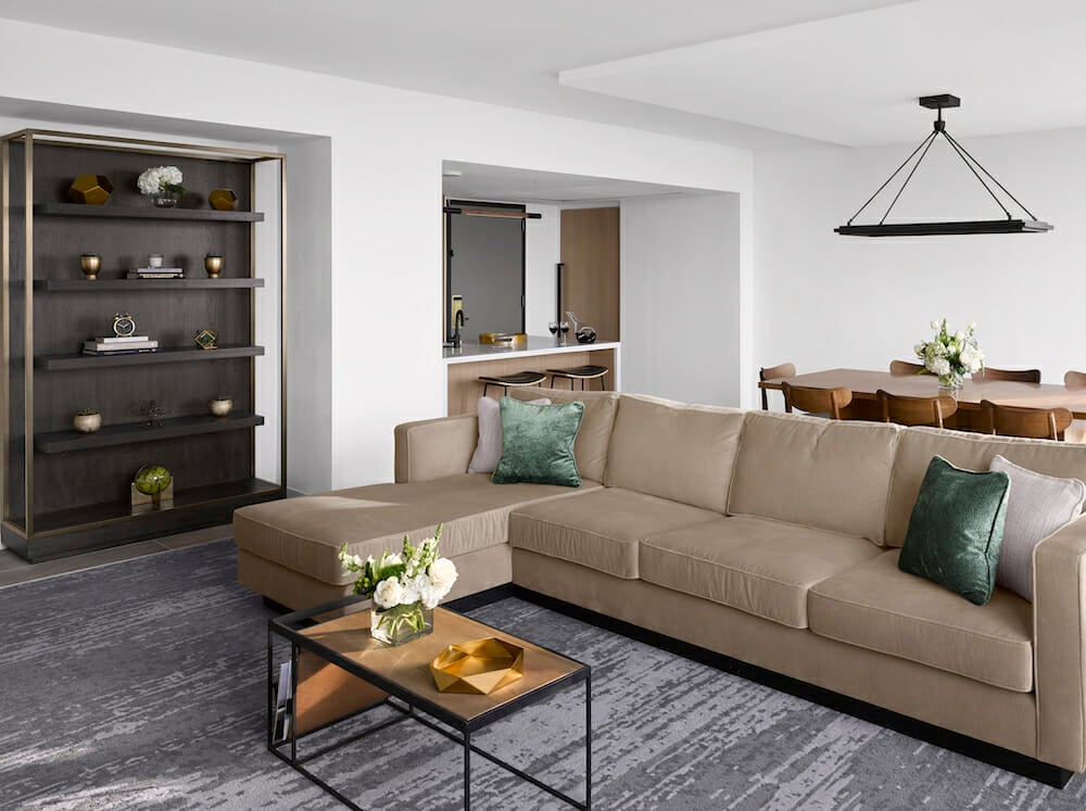 Spacious Presidential Suite living room with floor to ceiling windows, tan sectional in seating area and dining table behind it.