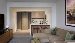 Spacious Presidential Suite living room with floor to ceiling windows, tan sectional in seating area and dining table behind it.