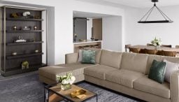 Spacious Presidential Suite living room with floor to ceiling windows, tan sectional in seating area and dining table behind it.